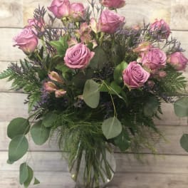 Pink roses in a clear glass vase with mixed greenery