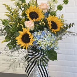 Sunflowers, pale roses, and blue hydrangeas in a striped ribbon vase