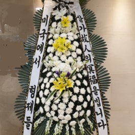 Standing funeral wreath with white and yellow flowers and Korean condolence ribbons
