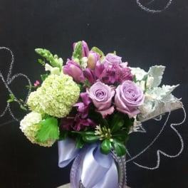 Lavender roses and purple flowers in a glass vase with a ribbon