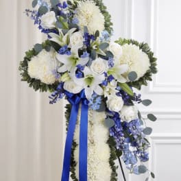 Standing floral cross with white flowers, blue accents, and a blue ribbon