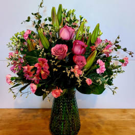 Pink roses and lilies arranged in a green glass vase