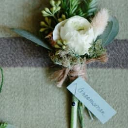 White boutonniere with greenery and a small feather accent