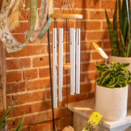 Silver wind chime hanging in front of a brick wall with potted plants nearby