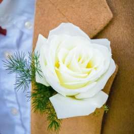 White rose boutonniere with green sprigs on a brown lapel
