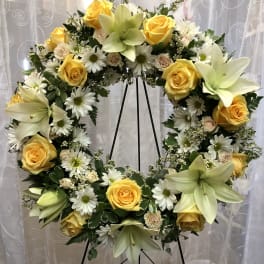 Large floral wreath with yellow roses, white daisies, and pale lilies on a stand