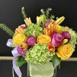 Colorful bouquet of roses, hydrangeas, and lilies in a square glass vase