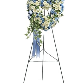 Heart-shaped standing wreath of white roses and blue flowers with ribbon on a metal easel