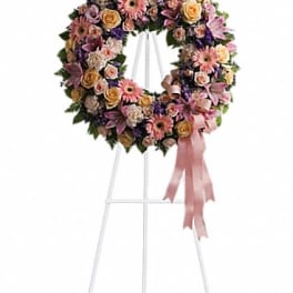 Pastel wreath of pink gerberas, roses, and lilies on a white standing easel with a pink ribbon.