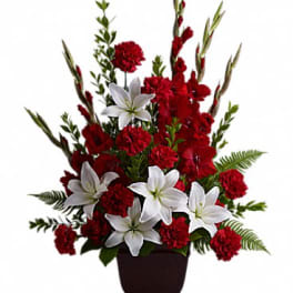 Tall arrangement of red flowers and white lilies in a dark square vase