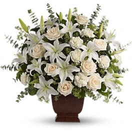 Large white lilies, cream roses, and carnations arranged in a dark pedestal vase.