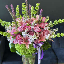 Pink roses and lilies arranged in a clear glass vase with green hydrangea and purple accents