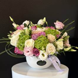 Mixed pink, white, and cream flowers arranged in a white bowl vase
