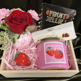 Gift box with a red rose, pink flowers, candy, and a pink candle