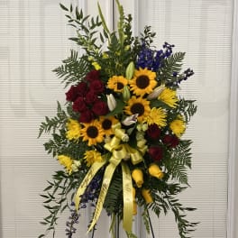 Standing floral spray with red roses, sunflowers, and yellow ribbon