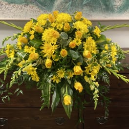 Large yellow floral arrangement with roses and daisies on a wooden casket