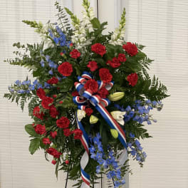 Standing floral spray with red carnations, blue flowers, and white blooms