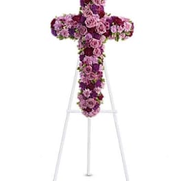 Tall standing floral cross of pink and purple blooms on a white easel