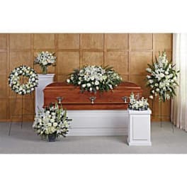 Funeral set with white floral casket spray, standing sprays, wreath, and arrangements around a wooden casket