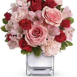Low arrangement of pink and red roses with pale carnations in a clear glass cube vase
