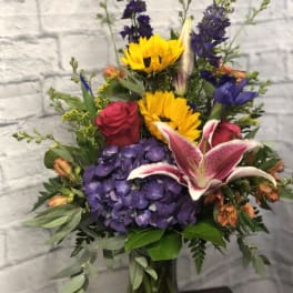Mixed bouquet with sunflowers, roses, lilies, and purple hydrangeas in a glass vase