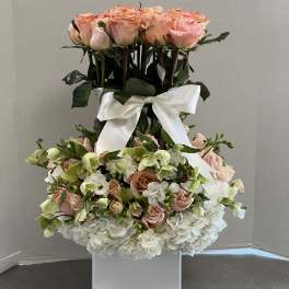 Tall floral arrangement of pink roses and white hydrangeas in a white vase with a ribbon
