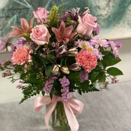 Pink roses and mixed flowers arranged in a glass vase with a pink ribbon.