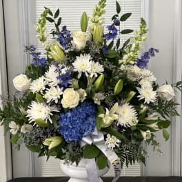 Large white and blue floral arrangement in a white urn vase