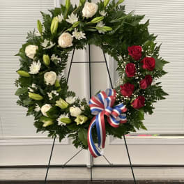 Floral wreath with red and white roses, lilies, and a tricolor ribbon on an easel