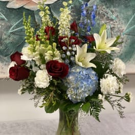 Mixed bouquet in a glass vase with red roses, white lilies, and blue hydrangea