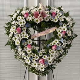 Heart-shaped floral wreath with white daisies, pink roses, and lilies on an easel
