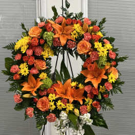 Large floral wreath with orange lilies, roses, and yellow blooms on a stand
