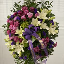 Standing floral wreath with white lilies, pink roses, and purple ribbon