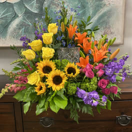 Colorful mixed bouquet with sunflowers, roses, lilies, and purple blooms in a glass vase