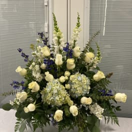 Large floral arrangement with white roses, blue flowers, and pale hydrangeas