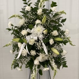 White floral standing spray with lilies, roses, and ribbon on an easel