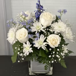 White roses and daisies in a square glass vase with blue flowers