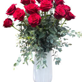 Red roses arranged in a white vase with trailing greenery