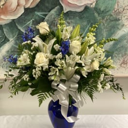 White lilies and roses arranged in a blue vase with a silver ribbon.