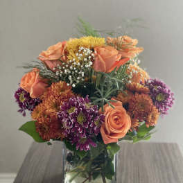Orange and purple mixed flowers arranged in a square glass vase