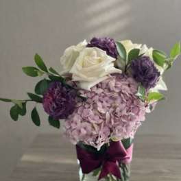 Pink hydrangea and white roses in a glass vase with purple blooms