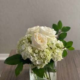 White roses and pale hydrangeas in a clear square vase