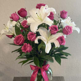 Pink roses and white lilies in a glass vase with a pink ribbon
