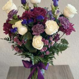 Bouquet of white roses, purple blooms, and a purple ribbon in a glass vase