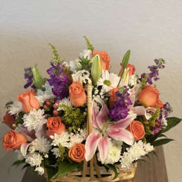 Basket arrangement of orange roses, pink lilies, and white daisies