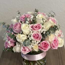 Pink and white roses arranged in a glass vase with eucalyptus
