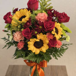 Bouquet of red roses, sunflowers, and carnations in a glass vase with orange ribbon