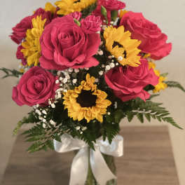 Bouquet of pink roses and yellow sunflowers in a glass vase with a white ribbon