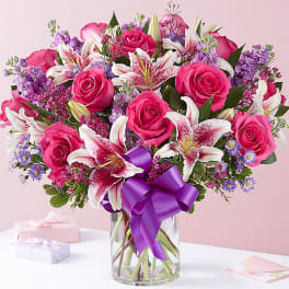 Pink roses and white lilies in a glass vase with a purple ribbon