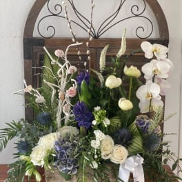 Mixed floral arrangement with white orchids, roses, and blue thistles in a wooden container
